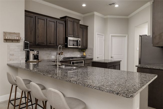 Kitchen featuring stainless steel appliances, dark brown cabinetry, dark stone counters, light backsplash, kitchen island and gas cooktop | Image 6
