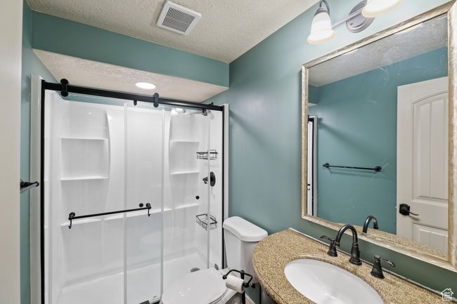 Bathroom with a textured ceiling, a shower stall, visible vents, toilet, and vanity | Image 27