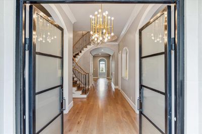 View from the double door Front Entry to the FOYER (32 X 7) with its wide planked hardwood flooring, painted crown/base molding, two glass/metal chandeliers, circular staircase (wood treads, painted risers, stained wood railing, wrought iron spindles, carpet runner), 3 wall staircase sconces, domed two story ceiling, under stairway storage closet, elevator and access to formal Living and Dining rooms, Powder Room, Library, Wet Bar and Family Room beyond. | Image 3