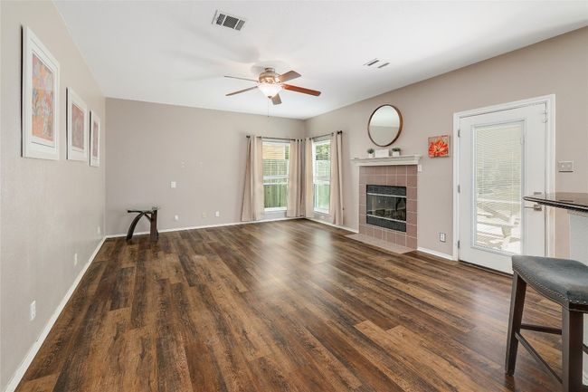 Unfurnished living room with baseboards, a ceiling fan, visible vents, dark wood finished floors, and a tile fireplace | Image 4
