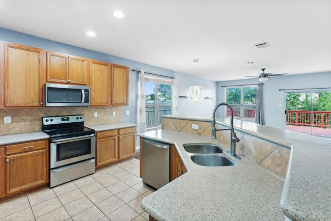 Kitchen with stainless steel appliances, decorative backsplash, light tile patterned floors, decorative light fixtures, and brown cabinets | Image 16