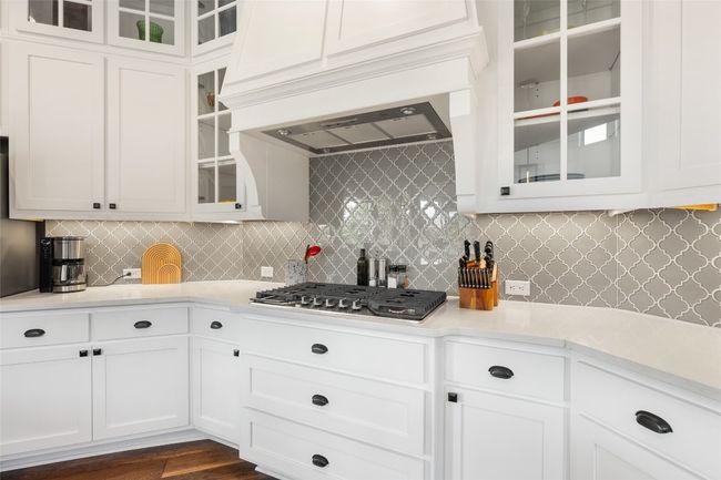 Kitchen featuring stainless steel gas stovetop, light countertops, decorative backsplash, and white cabinets | Image 14