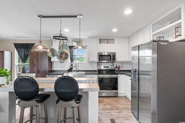 Kitchen with stainless steel appliances, open shelves, decorative backsplash, a textured ceiling, and white cabinets | Image 10