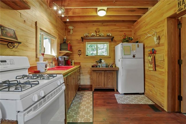 Kitchen featuring white appliances, a sink, wood walls, dark wood-style floors, and beam ceiling | Image 13