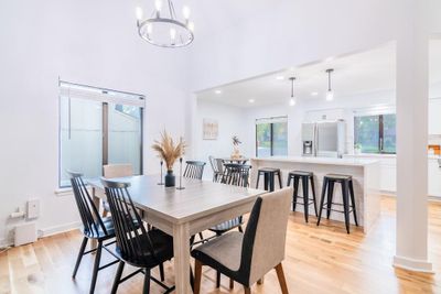 Dining room with a healthy amount of sunlight, an inviting chandelier, a towering ceiling, and light hardwood / wood-style floors | Image 3