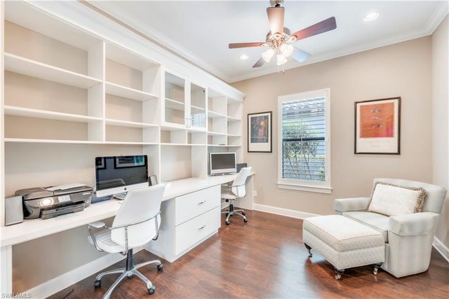 Office area with crown molding, dark wood finished floors, baseboards, ceiling fan, and built in desk | Image 18