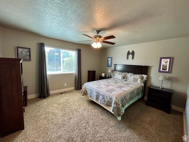 Bedroom with a textured ceiling, light carpet, baseboards, and a ceiling fan | Image 13