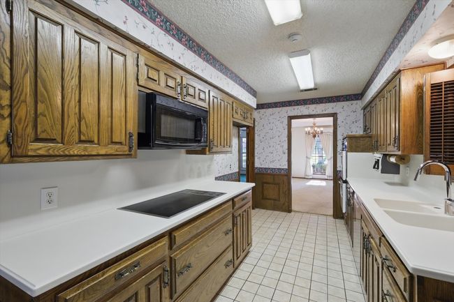 Kitchen with wallpapered walls, a sink, black appliances, a textured ceiling, and a notable chandelier | Image 9