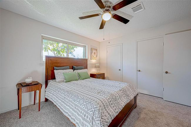 Roomy secondary bedroom features a ceiling fan, and ample natural light from a large window. It includes two closets and neutral new carpeting. | Image 25