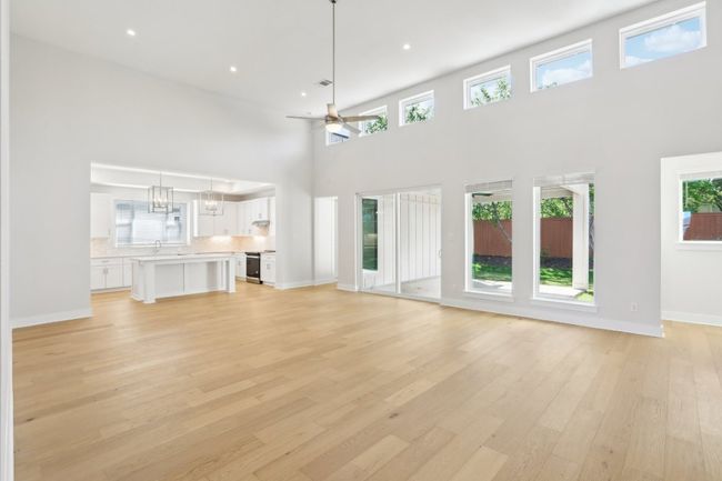 Unfurnished living room featuring baseboards, a high ceiling, light wood finished floors, ceiling fan with notable chandelier, and a sink | Image 7