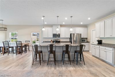 Kitchen with a breakfast bar, white cabinetry, light wood-type flooring, and stainless steel appliances | Image 2