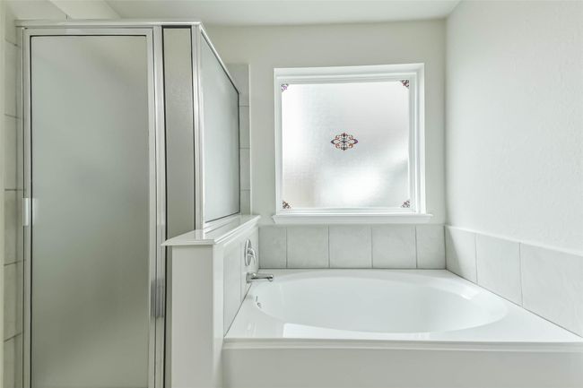 Experience spa-like luxury in this primary suite with a comfortable soaking tub, a glass-enclosed shower and large window for natural lighting. | Image 21