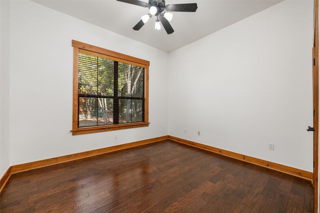 This front-facing secondary bedroom features large windows with views of the natural surroundings, filling the space with light. The warm wood trim and flooring provide a welcoming canvas for personalization. | Image 17