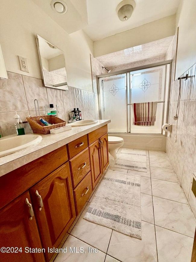 Full bathroom featuring tile walls, vanity, shower / bath combination with glass door, and toilet | Image 12