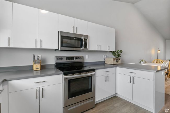 Kitchen with lofted ceiling, light wood-style floors, white cabinets, a peninsula, and appliances with stainless steel finishes | Image 16
