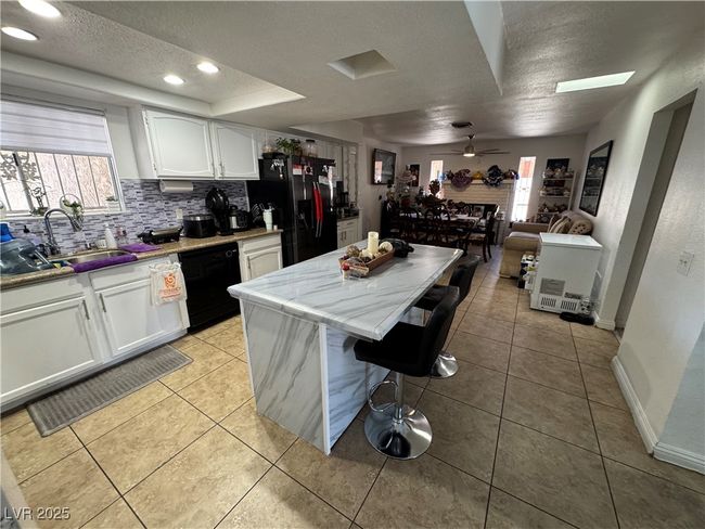Kitchen featuring black appliances, a sink, a textured ceiling, white cabinets, and a kitchen island | Image 5