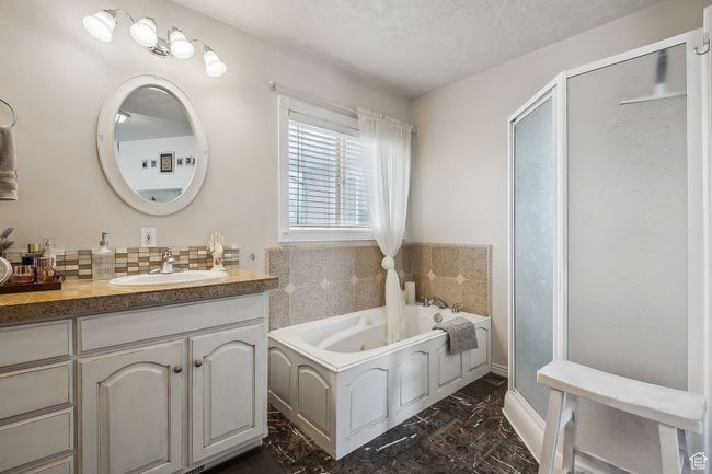 Full bath featuring a stall shower, decorative backsplash, marble finish floor, a tub with jets, and vanity | Image 24