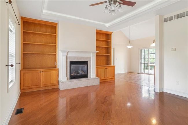 Unfurnished living room featuring built in shelves, a tiled fireplace, a ceiling fan, baseboards, and visible vents | Image 9