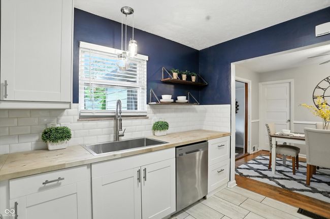 kitchen with stainless steel dishwasher, wooden counters, white cabinetry, tasteful backsplash, and decorative light fixtures | Image 6