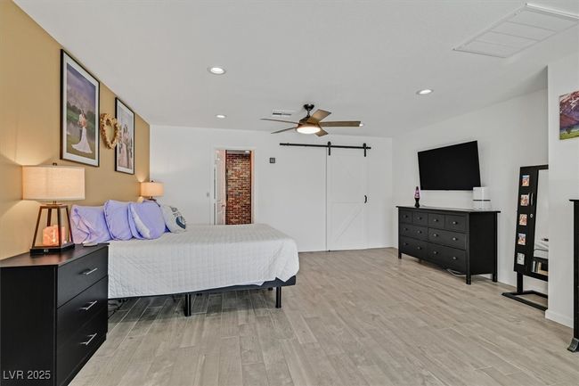 Bedroom featuring light wood-type flooring, visible vents, recessed lighting, a barn door, and ceiling fan | Image 14