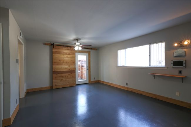 Unfurnished living room featuring finished concrete floors, a barn door, and a ceiling fan | Image 13