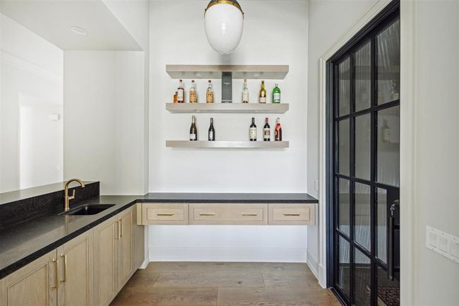 Perfectly positioned off the formal living room, this exquisite wet bar features sleek Black Misted honed quartzite countertops, white oak built-in shelves with art lighting, and direct access to the walk-in climate-controlled wine room, creating an ideal space for entertaining. | Image 28
