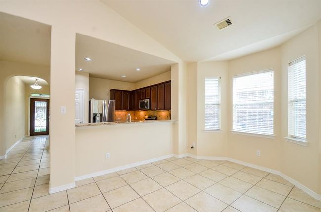 Bright open-concept kitchen and breakfast area with bay windows, featuring tiled floors, stainless steel appliances, and ample natural light from multiple windows. Adjacent hallway with elegant entrance door enhances the inviting atmosphere. | Image 14