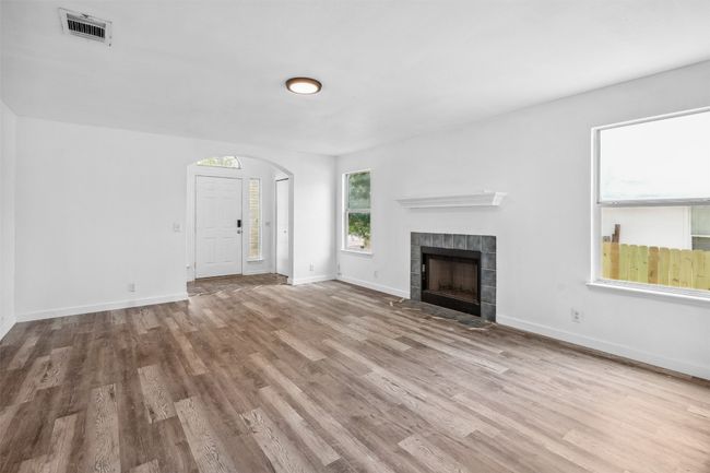 Unfurnished living room featuring arched walkways, baseboards, wood finished floors, a tile fireplace, and visible vents | Image 8