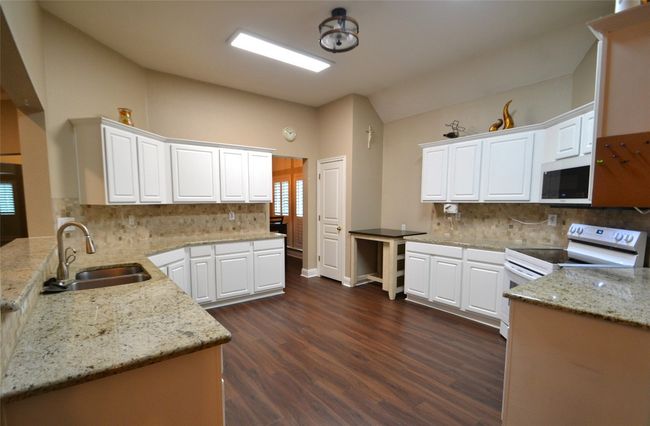 Kitchen with white appliances, vaulted ceiling, dark wood finished floors, tasteful backsplash, and white cabinetry | Image 9