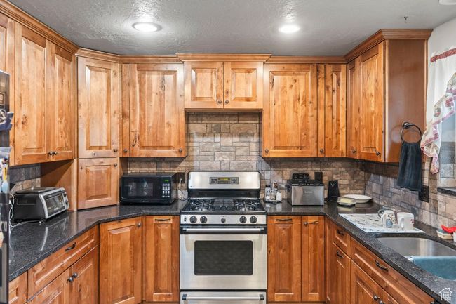 Kitchen featuring a toaster, backsplash, a sink, black microwave, and stainless steel range with gas stovetop | Image 11