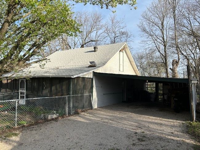View of property exterior featuring aphalt driveway, fence, roof with shingles, a sunroom, and an attached carport | Image 31