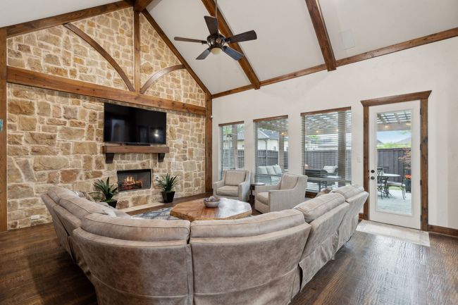 Living area with high vaulted ceiling, beamed ceiling, wood finished floors, ceiling fan, and a fireplace | Image 6