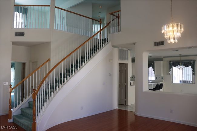 Staircase with a chandelier, a towering ceiling, wood finished floors, and arched walkways | Image 20