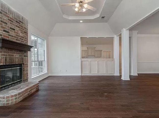 Unfurnished living room featuring a tray ceiling, dark wood-style flooring, a brick fireplace, crown molding, and ceiling fan | Image 6