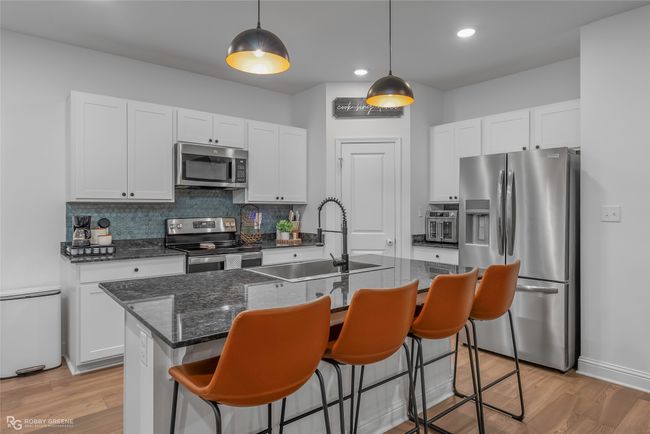 Kitchen featuring a kitchen bar, white cabinetry, appliances with stainless steel finishes, a sink, and backsplash | Image 10