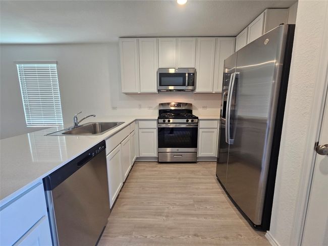 Kitchen featuring stainless steel appliances, light countertops, light wood finished floors, a sink, and white cabinetry | Image 6