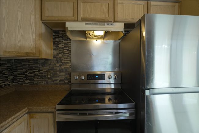 Kitchen with appliances with stainless steel finishes, light brown cabinetry, under cabinet range hood, decorative backsplash, and dark countertops | Image 7