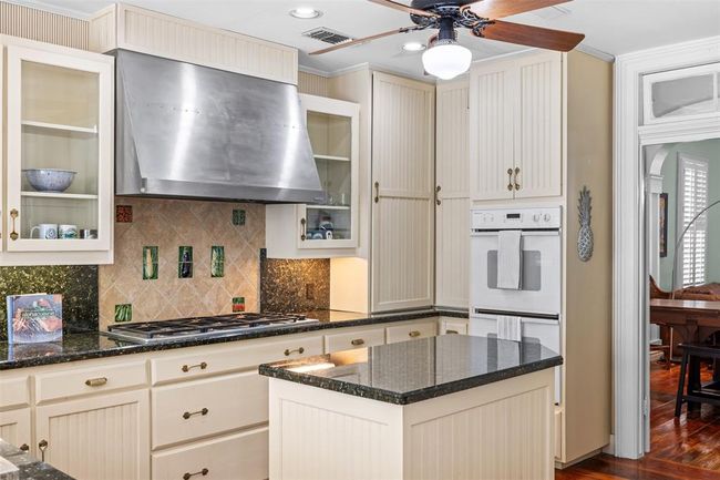 Rekindle your passion for cooking in this beautifully updated kitchen, featuring a six-burner gas range, dual ovens, a island, and plenty of workspaces. The kitchen boasts elegant beveled glass and beadboard cabinetry, stone countertops, rich hardwood flooring, a convenient pantry, and a charming historical transom entryway. | Image 10