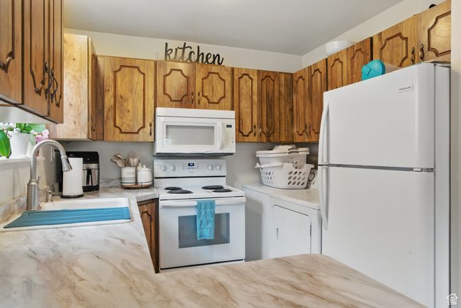 Kitchen with a sink, white appliances, brown cabinetry, light countertops, and washer / dryer | Image 28
