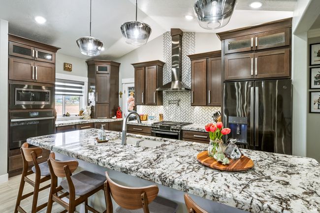 Kitchen with stainless steel appliances, wall chimney exhaust hood, lofted ceiling, backsplash, and glass insert cabinets | Image 25