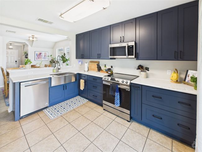 Kitchen featuring appliances with stainless steel finishes, a peninsula, light countertops, light tile patterned flooring, and arched walkways | Image 9