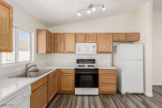 Kitchen with light countertops, white appliances, lofted ceiling, and a sink | Image 4