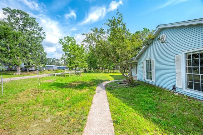 Charming side view of the home, featuring a lush lawn, mature trees, and a welcoming walkway. Perfect for enjoying outdoor relaxation in a serene setting. | Image 6