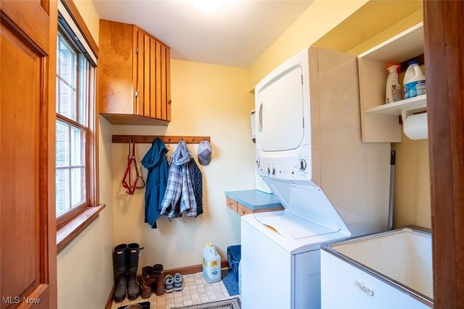 Main laundry room with cabinet space, stacked washer / drying machine, healthy amount of natural light, and tile patterned flooring | Image 15