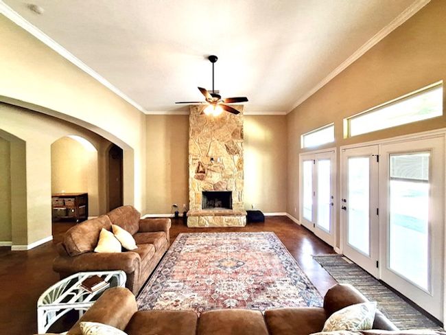 Living area with arched walkways, baseboards, wood finished floors, ceiling fan, and crown molding | Image 5
