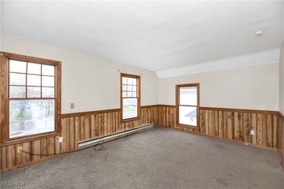 Spare room with carpet flooring, wood walls, vaulted ceiling, and a baseboard heating unit | Image 3