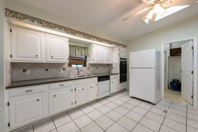 Kitchen with white appliances, dark countertops, a ceiling fan, decorative backsplash, and white cabinetry | Image 19
