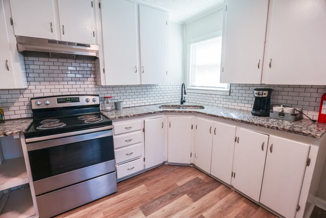Kitchen with under cabinet range hood, electric range, a sink, white cabinets, and light wood-type flooring | Image 9