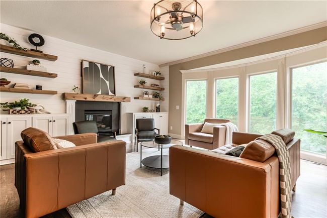 Living area featuring a fireplace, plenty of natural light, light wood finished floors, a chandelier, and wooden walls | Image 15