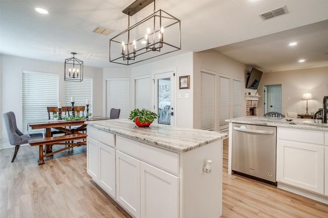 Kitchen featuring stainless steel dishwasher, a chandelier, light wood-type flooring, a kitchen island, and white cabinets | Image 18